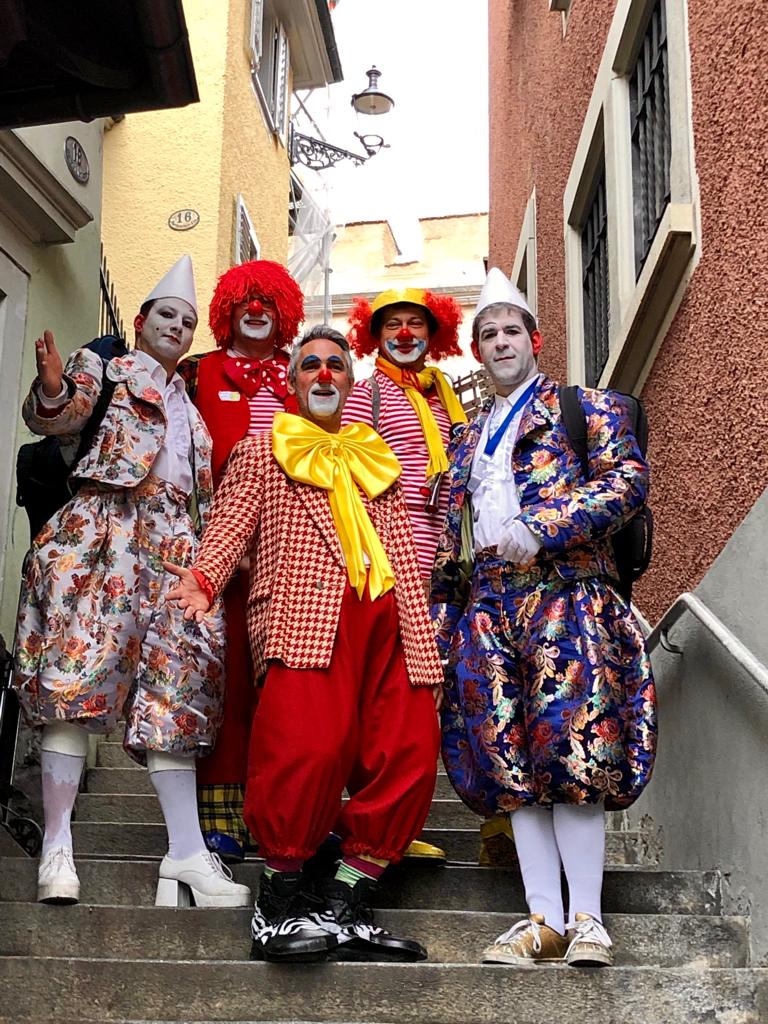 Sujet 2019: Clowns — fünf Musiker in bunten Clownskostümen auf einer Gassentreppe